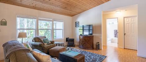 A spacious living room with a wooden ceiling, a large window, a television, and a fireplace.