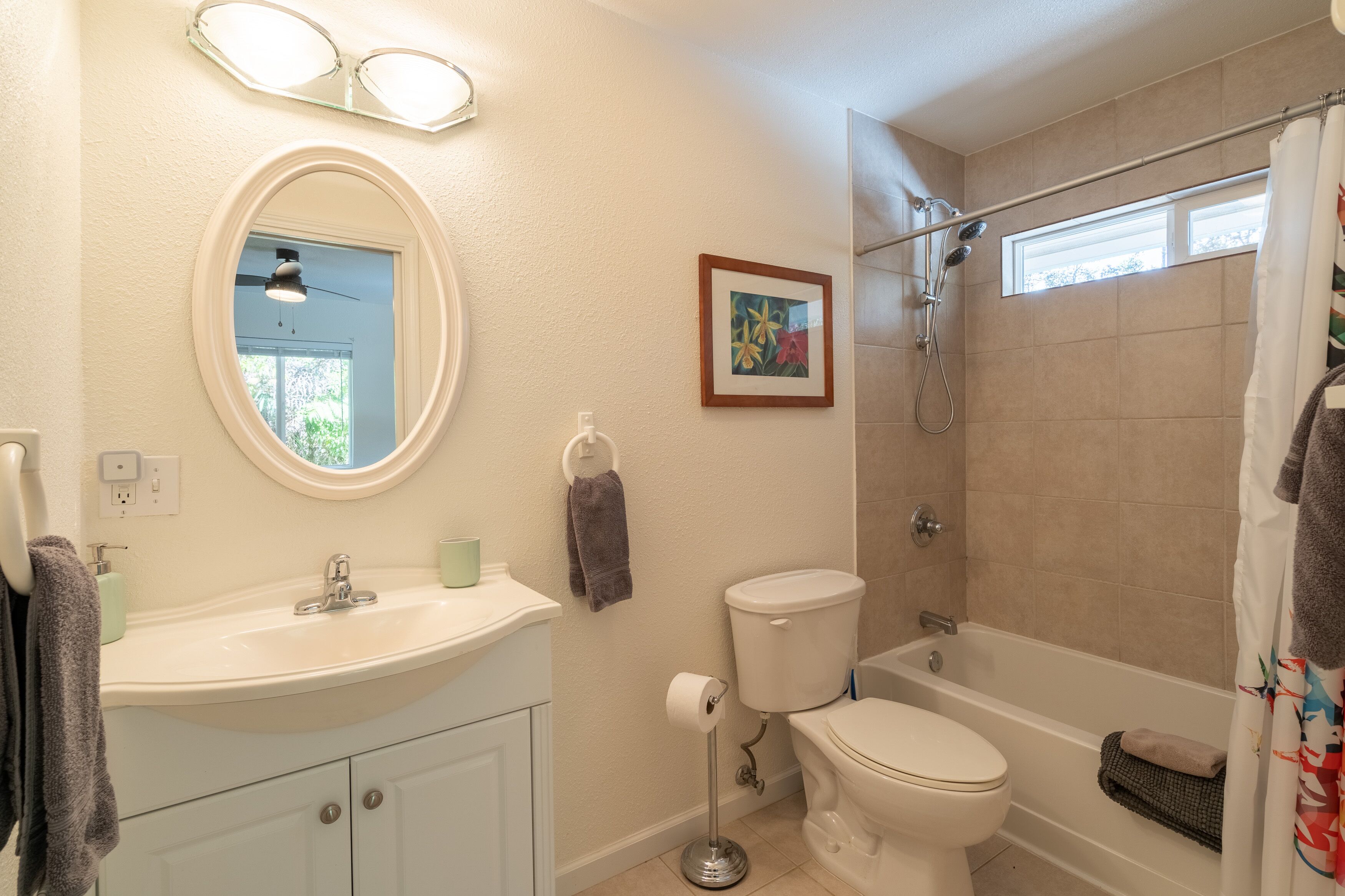 A bathroom with a sink, toilet, and bathtub. There is a framed picture on the wall and a window above the bathtub.