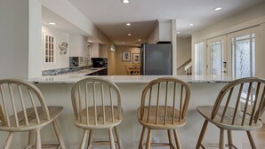 Une cuisine moderne avec un plan de travail en marbre, des chaises en bois et un grand réfrigérateur.