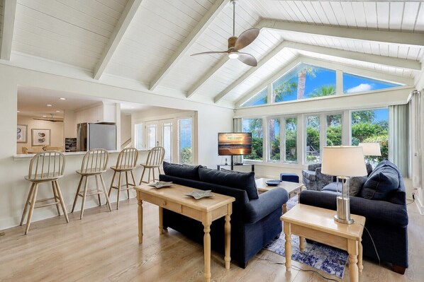 A spacious living area with a high ceiling, a dining area with wooden chairs, a sofa, and a television.