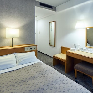 Une chambre d’hôtel comprenant un lit, une table de chevet, une lampe, un miroir et un petit bureau avec une chaise.