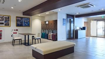 Um hall de hotel com área de estar, cozinha compacta e espaço para guardar malas.