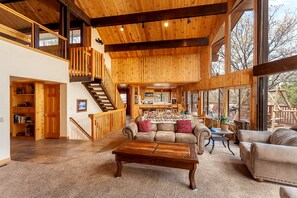 Un salón amplio con techo de madera, una escalera y ventanas grandes.