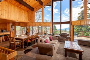 Un interior de madera espacioso con comedor, asientos y grandes ventanales que ofrecen vistas al exterior.