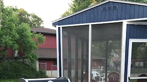 A Weber Genesis portable grill with a built-in cooler, positioned on a concrete patio adjacent to a blue shed with a glass door. - 3rd and Surf- 2 blocks from the lake, 1 block from the Legendary Surf Ballroom (Clear Lake)