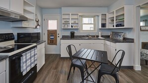 A modern kitchen with white cabinets, a black stove, and a dining table with two chairs. - 3rd and Surf- 2 blocks from the lake, 1 block from the Legendary Surf Ballroom (Clear Lake)