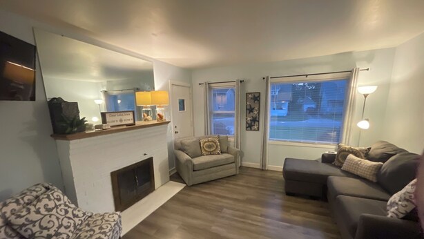 A living room with a fireplace, two sofas, a patterned armchair, and a large window with blinds. - 3rd and Surf- 2 blocks from the lake, 1 block from the Legendary Surf Ballroom (Clear Lake)