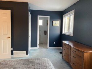 A room with dark blue walls, a white door, a wooden dresser, and a window. - Malagash Oceanside Vacation Home (Malagash Point)