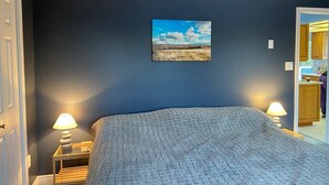 Un dormitorio con una cama grande, dos lámparas de noche, un cuadro en la pared y una puerta que da al baño.