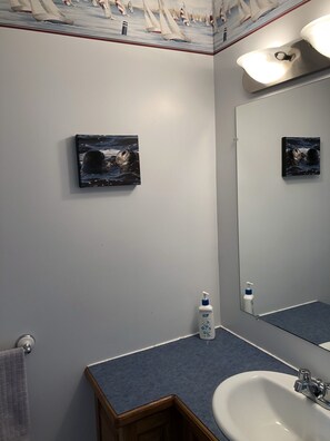 A bathroom with a large mirror, a sink, and two framed pictures on the wall. - Malagash Oceanside Vacation Home (Malagash Point)