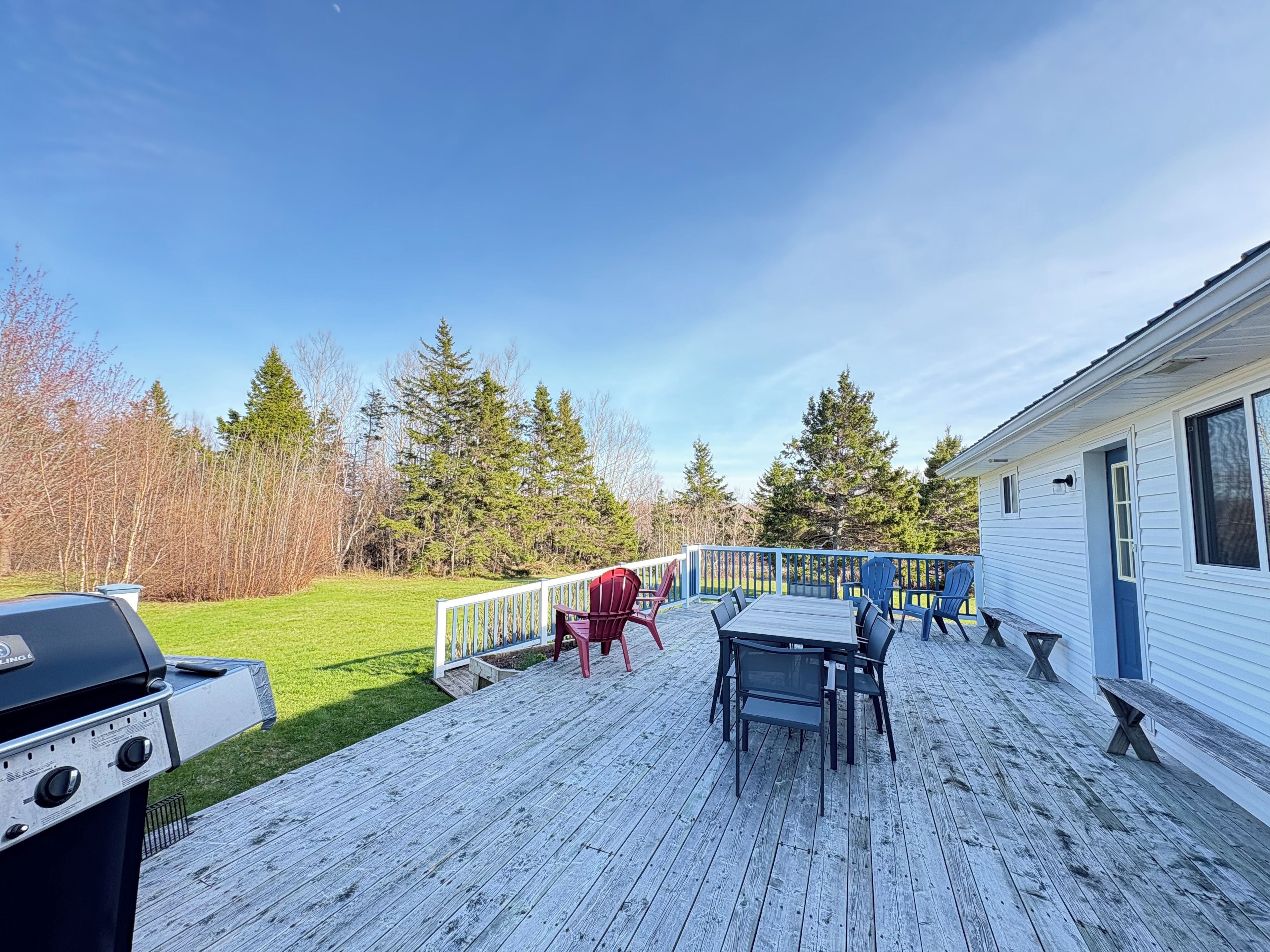 Une terrasse équipée d’un barbecue, de meubles d’extérieur et offrant une vue sur une zone boisée.