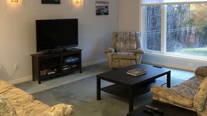Una sala de estar con televisión, dos sillones, una mesa de centro y una estantería.