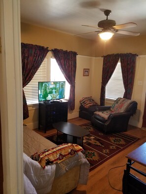 Relax in this cozy space with a sofa, coffee table, and television, surrounded by natural light and a ceiling fan.