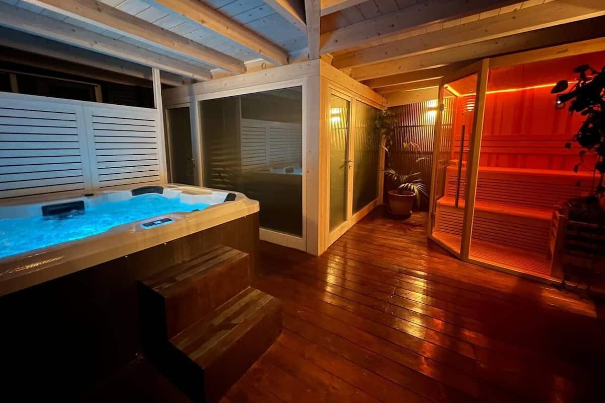 A spa area with a hot tub, wooden flooring, and a glass door leading to a red-lit room.