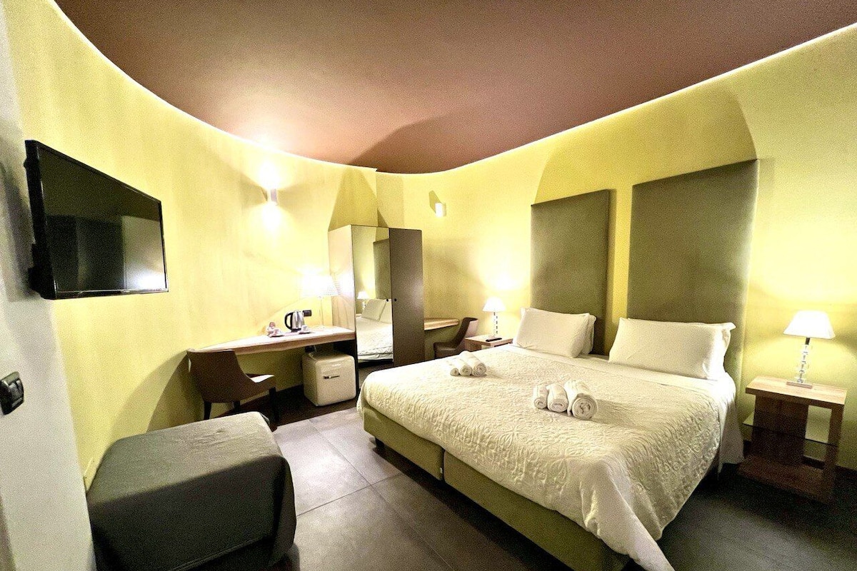 A hotel room with a bed, a desk, a chair, a TV, and a lamp.