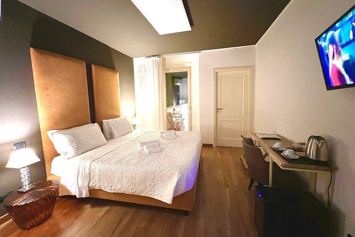 A hotel room with a large bed, a desk, a chair, a TV, and a lamp.
