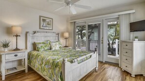 A bedroom with a bed, nightstands, a dresser, a ceiling fan, a TV, and a balcony with a view of trees. - The Sand Trap in South Bethany: Steps from the ocean!  Hot Tub! Captain's walk! (Bethany Beach)