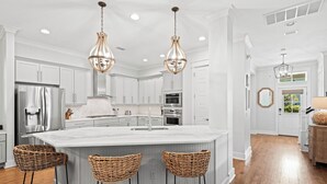 A modern kitchen with white cabinetry, a large island with bar stools, stainless steel appliances, and pendant lighting. - Exquisite 4-Bedroom WaterColor Retreat with Bikes, Golf Cart, and Pet-Friendly Amenities! (Santa Rosa Beach, Florida)