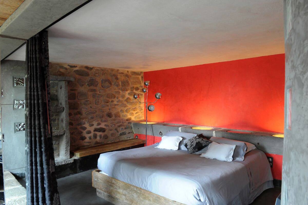 Ein Schlafzimmer mit Steinsandsteinwand, einer roten Akzentwand, einem Bett mit Kissen, einem Nachttisch und einer Lampe.