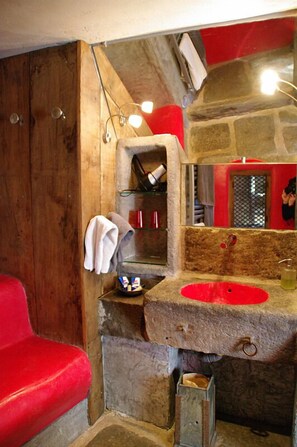 A rustic bathroom with a stone sink, wooden walls, and a red chair. - La Ferme de Moulhac (Laguiole)