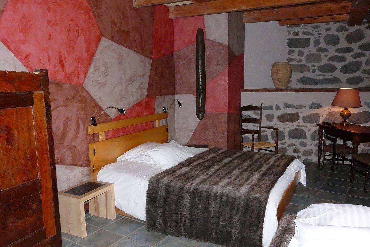 Ein Schlafzimmer mit einem hölzernen Bett, einem kleinen Nachttisch, einer Steinsäule und einem Steinkamin.