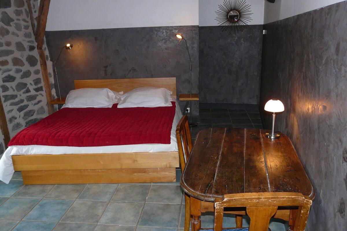 Ein Schlafzimmer mit einem hölzernen Bett, einer roten Decke, einem Holztisch und zwei Wandlampen.