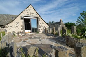 A stone cottage with a large open door leading to a room with a bed. - La Ferme de Moulhac (Laguiole)