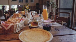 Une table en bois dressée pour le petit-déjeuner, avec du pain, des viennoiseries, un verre de jus d’orange et une tasse de thé.