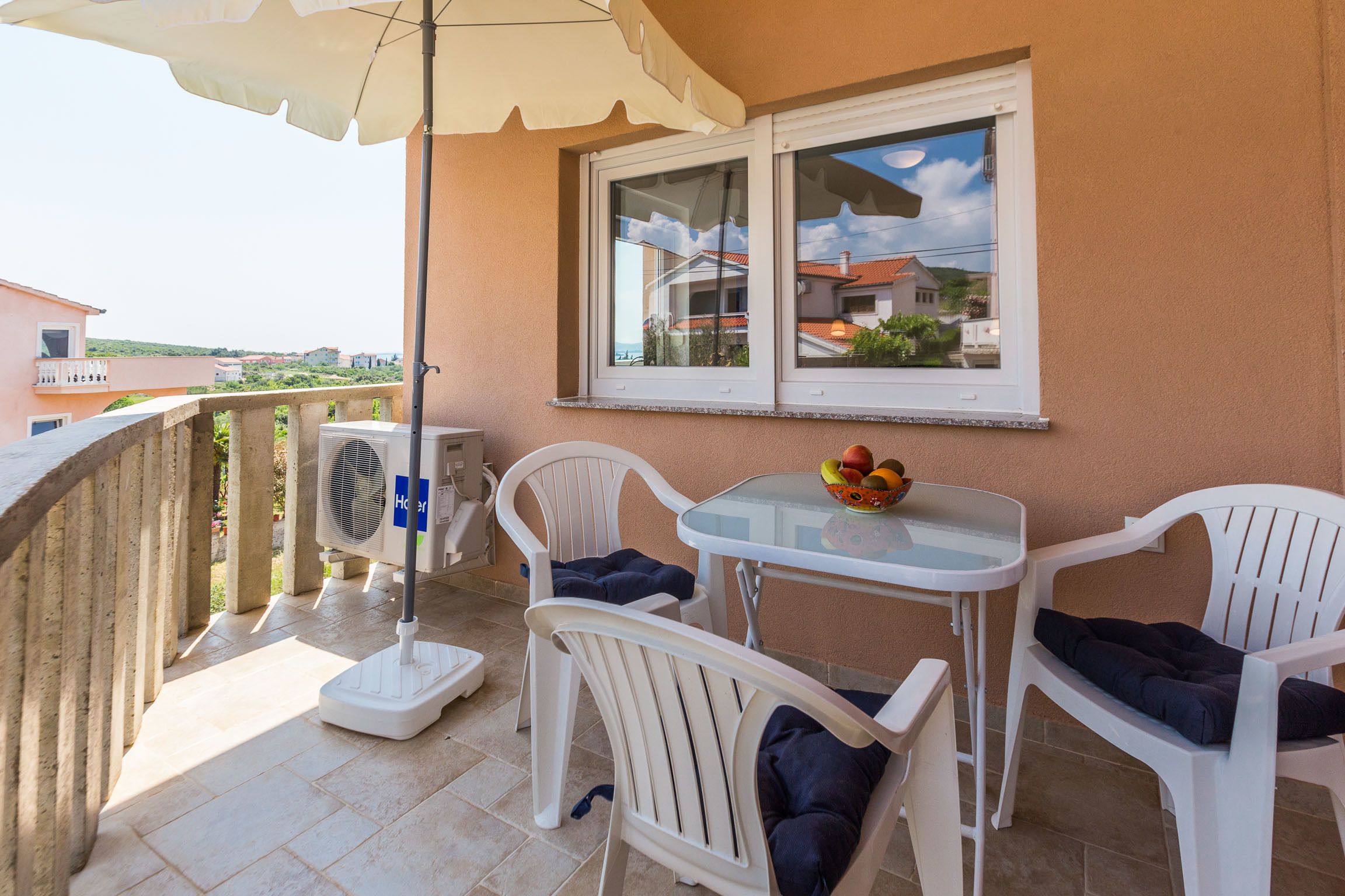 A balcony with a table and chairs, a fan, and a window overlooking a residential area.