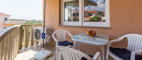 A balcony with a table and chairs, a fan, and a window overlooking a residential area.