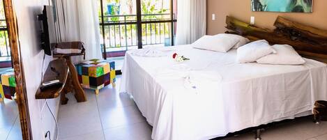 A hotel room with a bed, a TV, a balcony with a view of greenery, and a red chair.