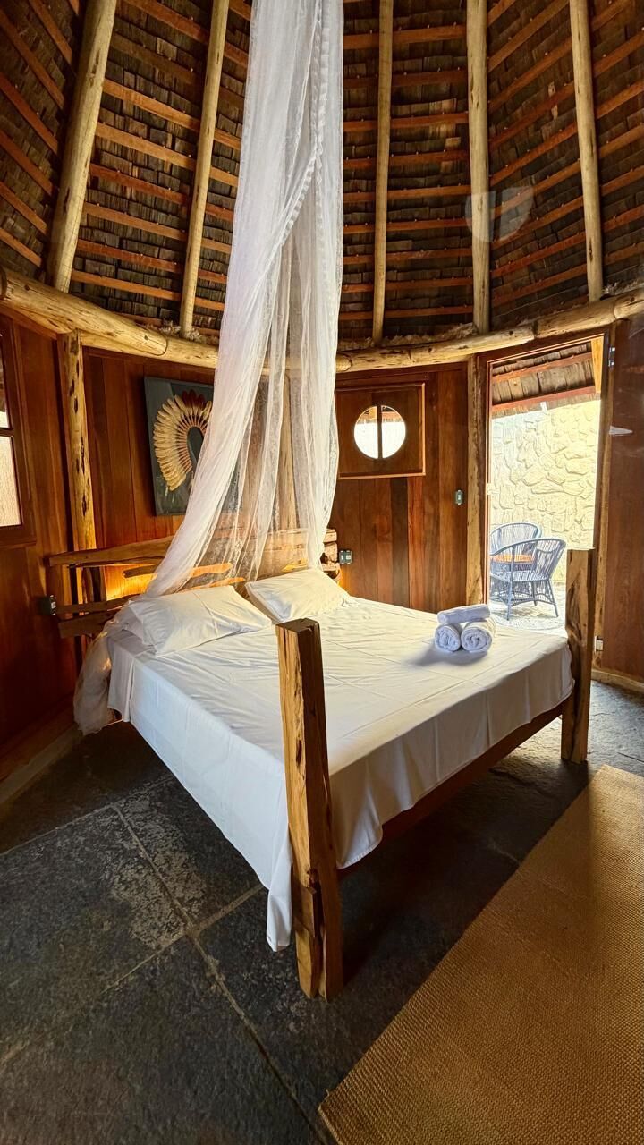 A wooden bed with a canopy in a rustic room with stone flooring and a stone wall.