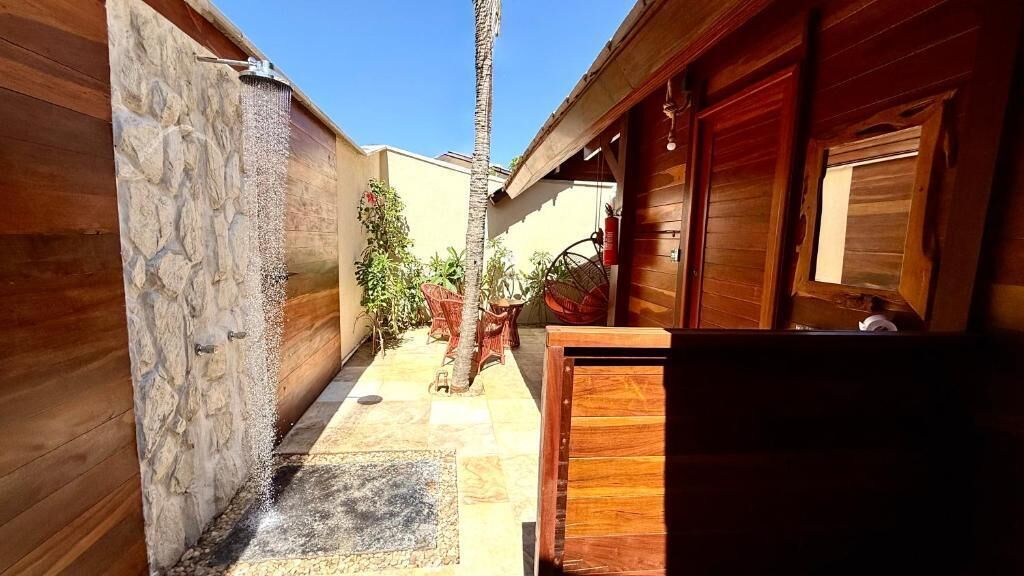 Un estrecho pasillo exterior con un muro de piedra a un lado, una puerta de madera al otro y una pequeña palmera en el centro.