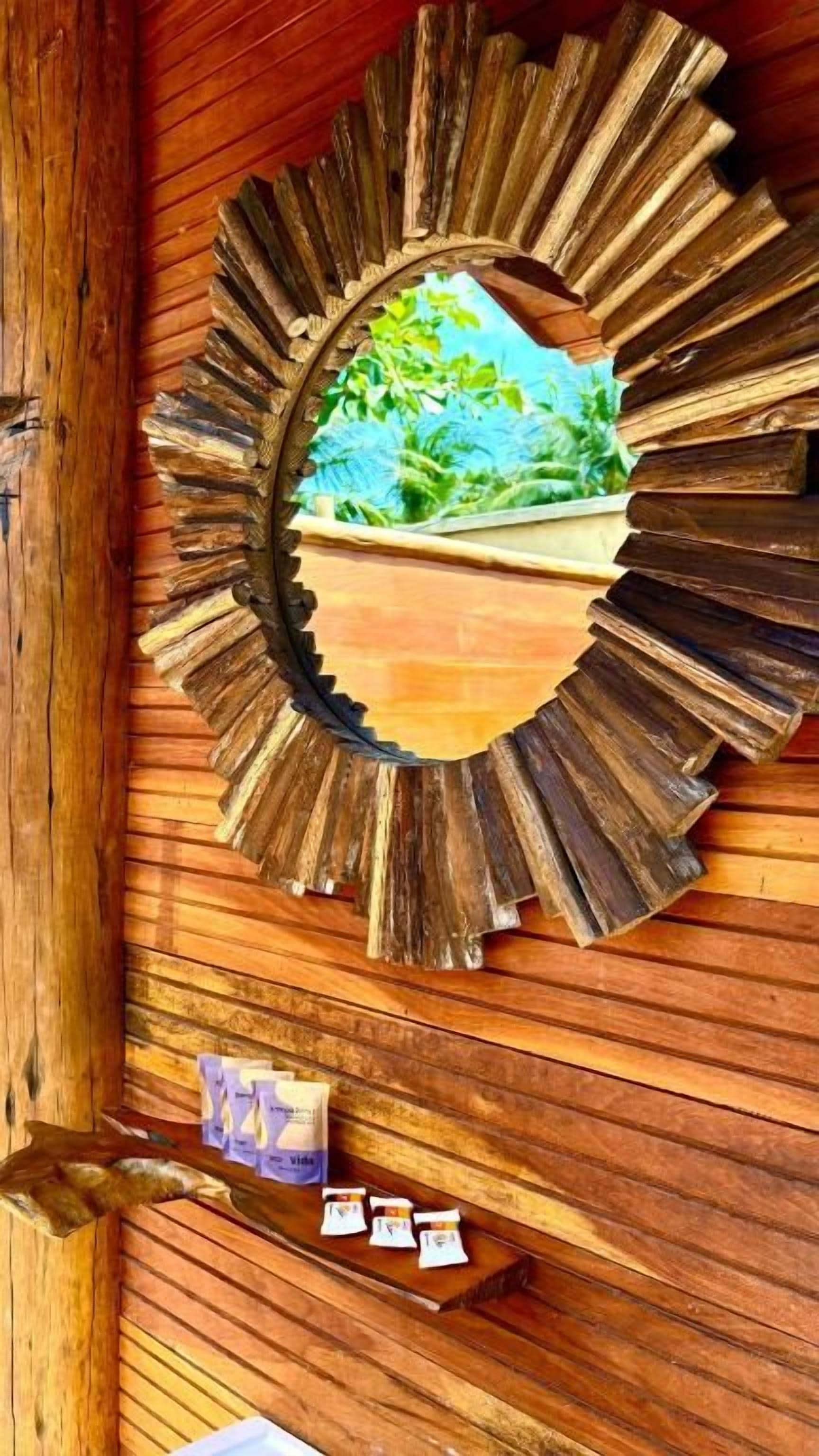 A wooden wall with a circular mirror reflecting greenery.