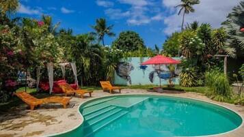 Una piscina con sillas de descanso, rodeada de vegetación tropical y un cielo azul despejado.