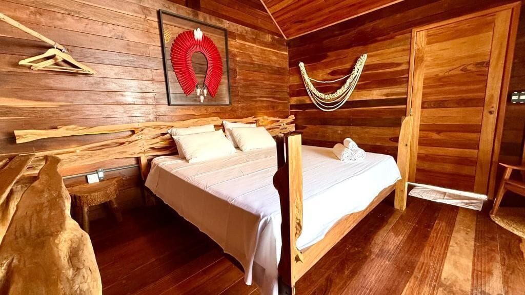A wooden cabin room with a bed, a hammock, and a wall-mounted decorative item.