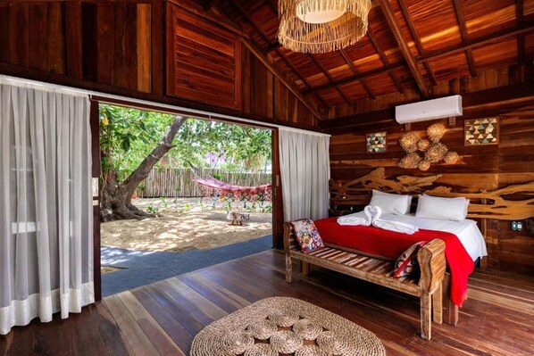 Una habitación de madera con una cama, un tapete tejido para el suelo y vistas a un jardín.