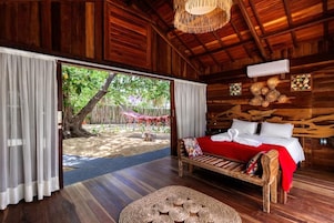 Quarto de madeira com uma cama, tapete de palha no chão e vista para um jardim.