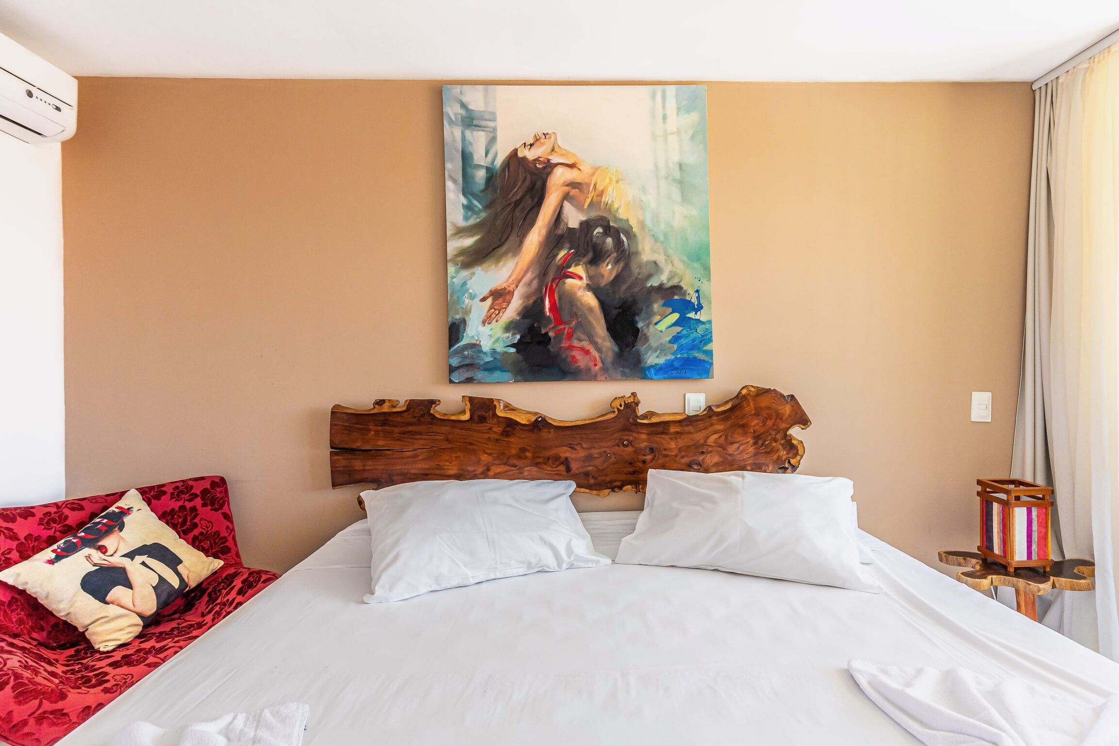 A hotel room with a large bed, a wooden headboard, a red sofa, and a painting on the wall.