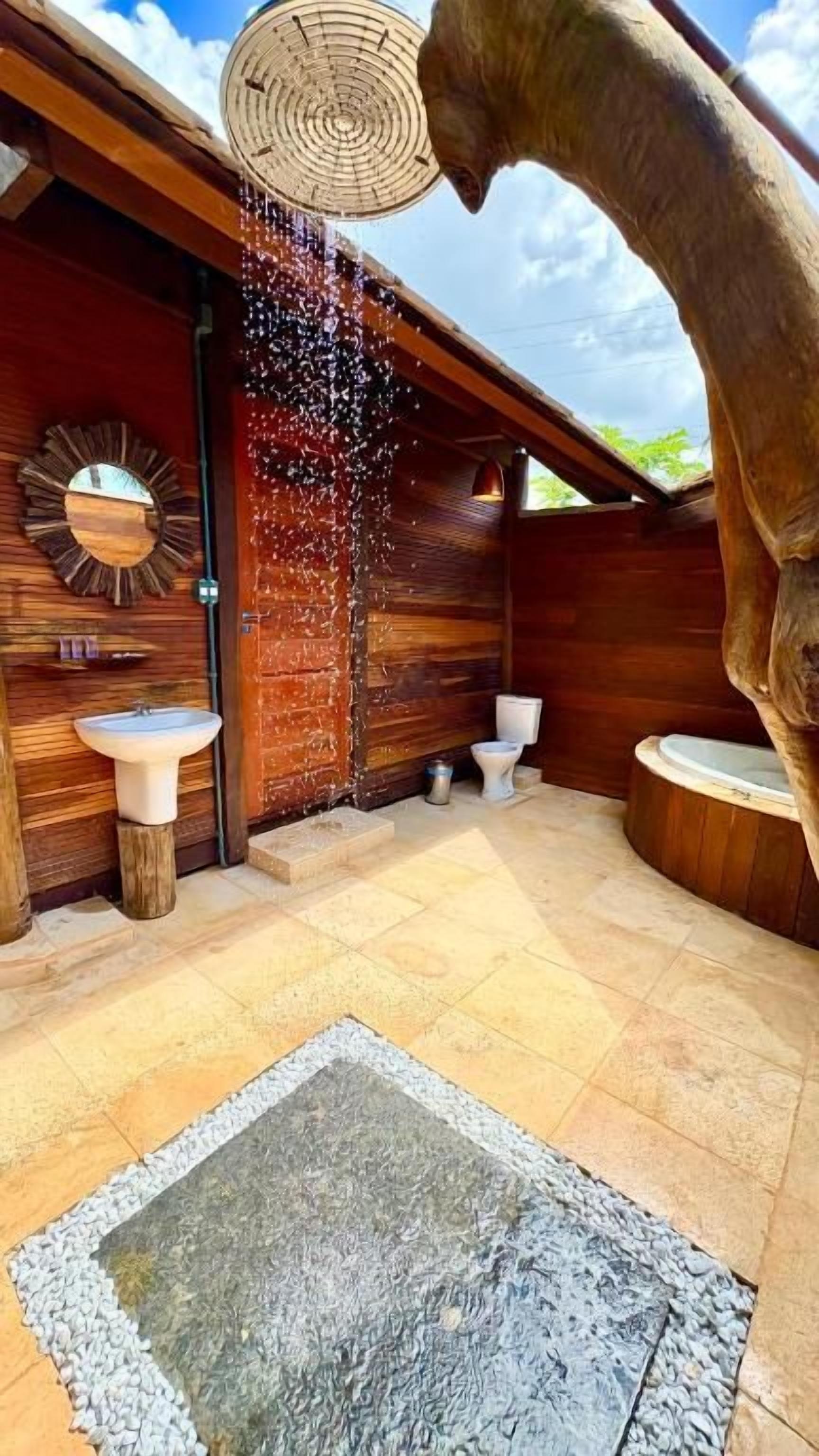 A rustic bathroom with wooden walls, two sinks, a toilet, and a unique water feature.