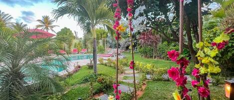 Un jardín exuberante con piscina, palmeras y flores coloridas.
