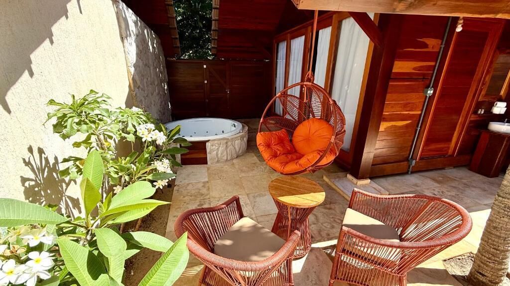 A patio with wicker furniture, a hot tub, and a wooden structure.