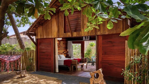 A wooden cabin with a bed, a small table, and a bench. - Xainã Pousada de Charme (Caucaia)