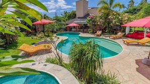 A swimming pool with lounge chairs and umbrellas, surrounded by lush greenery and a building with a tiled roof. - Xainã Pousada de Charme (Caucaia)