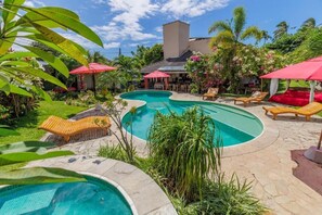 A swimming pool with lounge chairs and umbrellas, surrounded by lush greenery and a building with a tiled roof. - Xainã Pousada de Charme (Caucaia)