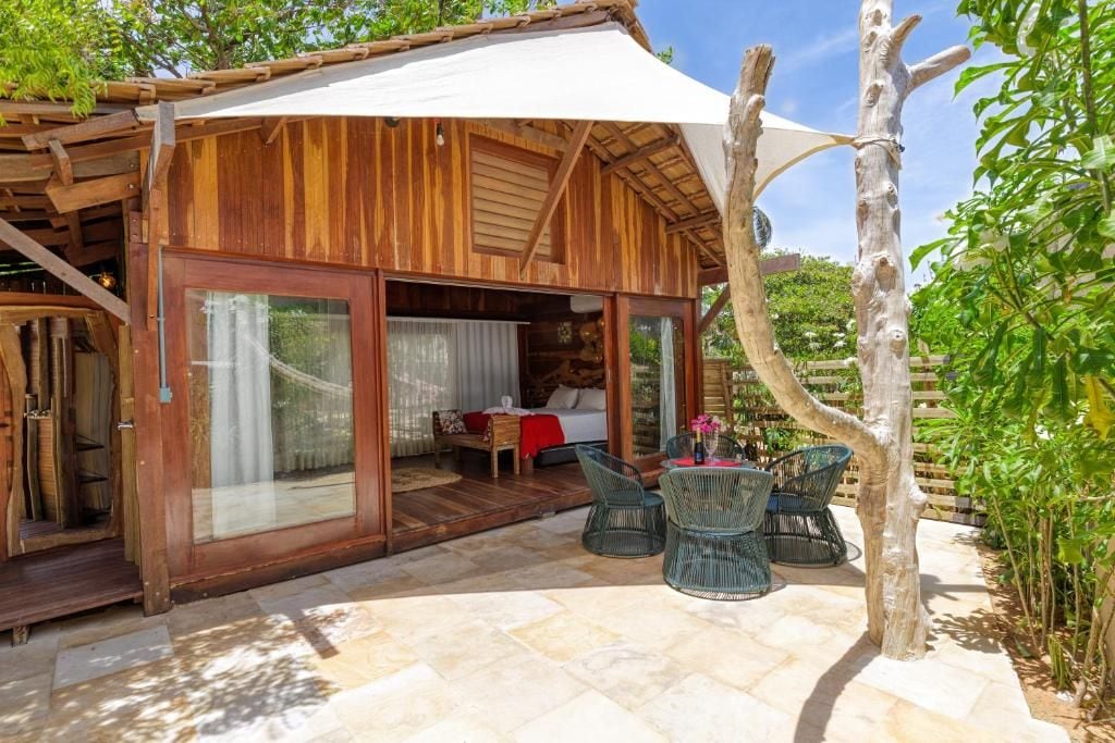A wooden cabin with a glass door entrance, a patio with chairs, and a small table.