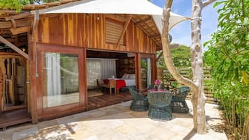 A wooden cabin with a glass door entrance, a patio with chairs, and a small table.