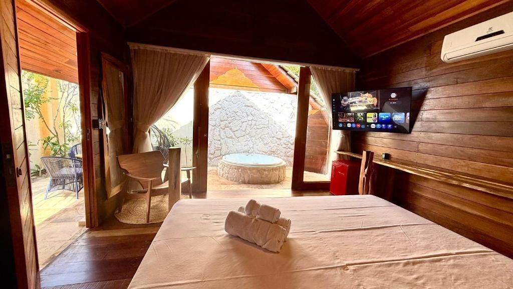 A room with a bed, a television, and a view of an outdoor area with a stone wall and a round table.