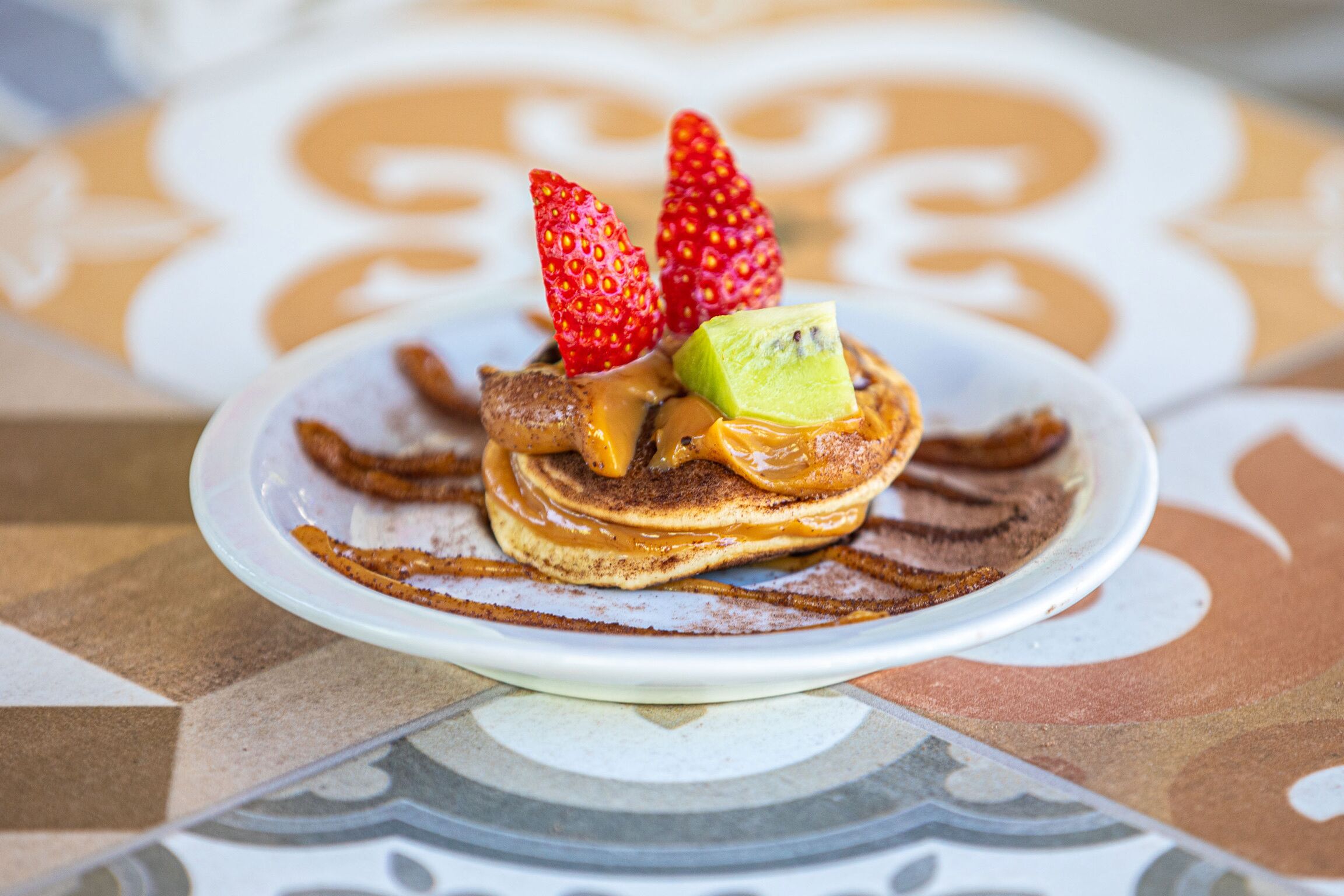 A plate of pancakes with strawberries and a slice of avocado on top.