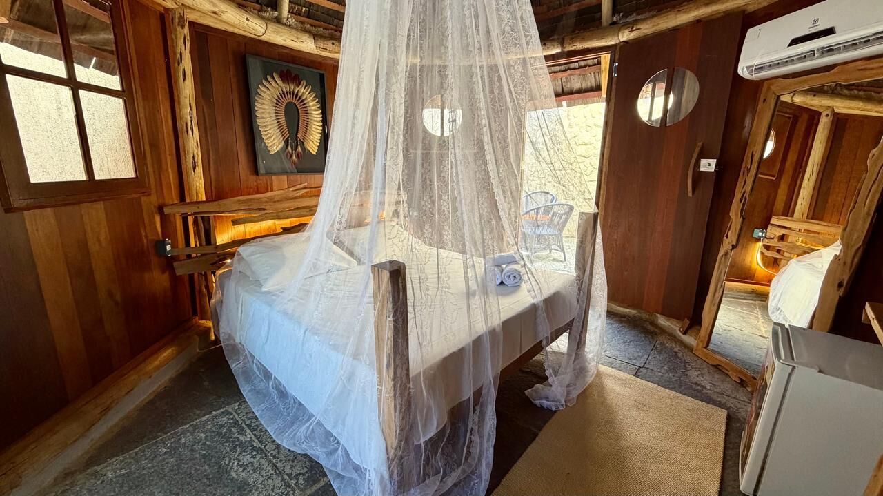 A room with a canopy bed, wooden walls, a decorative wall piece, and a small table with a chair.